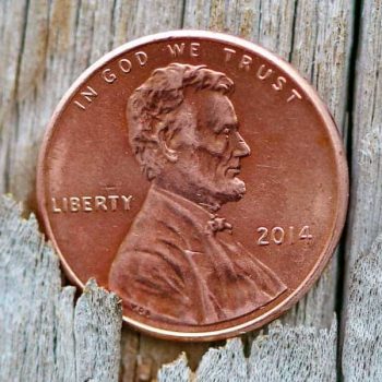 A penny falling through the cracks of a wooden floor, with Abe Lincoln's face up