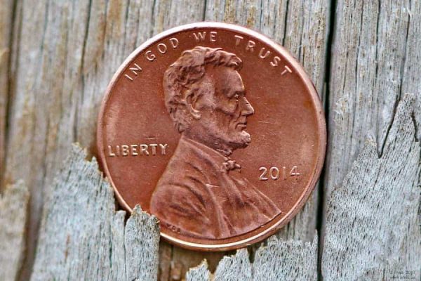 A penny falling through the cracks of a wooden floor, with Abe Lincoln's face up