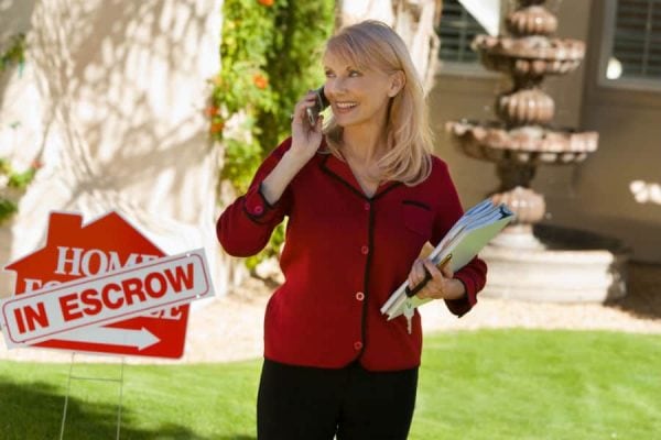 First Time Home Buyer Myths - Real Estate agent standing in front of a house in escrow sign.