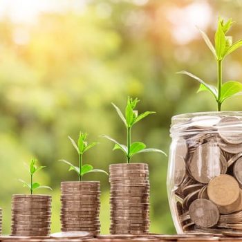 Three ascending stacks of quarters with new sprouts beside a jar of change sprouting