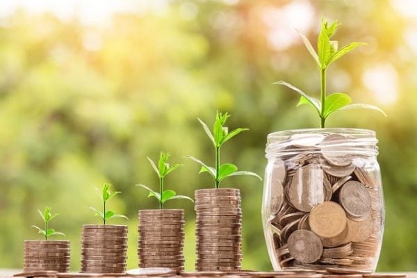 Three ascending stacks of quarters with new sprouts beside a jar of change sprouting