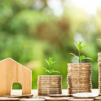 Three ascending stacks of quarters with new sprouts beside wooden home model