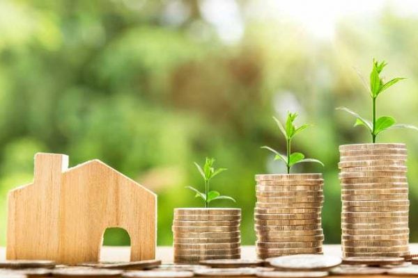 Three ascending stacks of quarters with new sprouts beside wooden home model