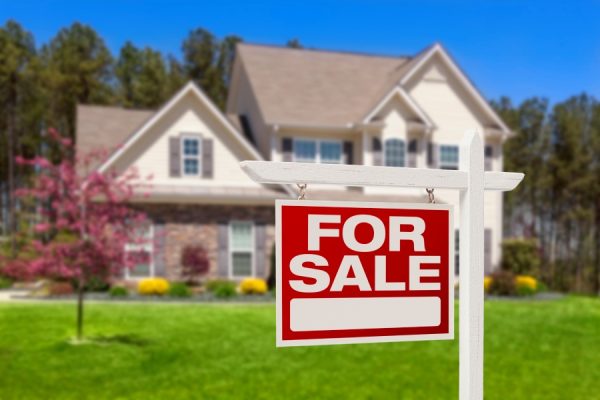 for sale sign in focus with a home for sale in the background