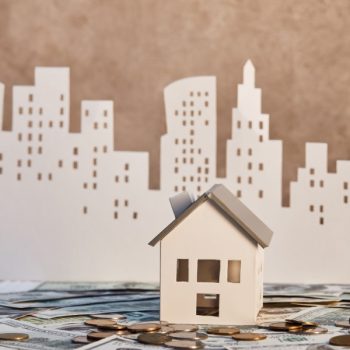 paper-house-in-paper-city-with-coins-and-bills-in-foreground