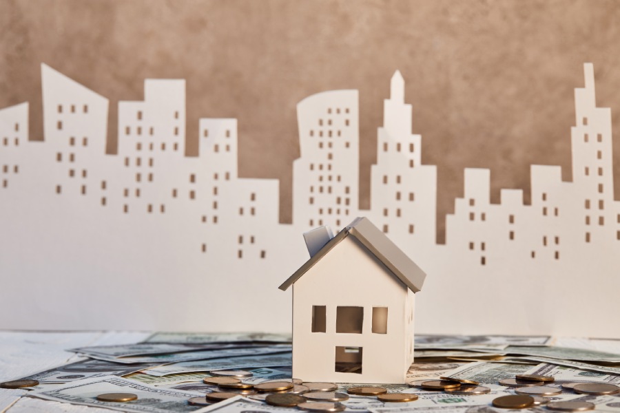 paper-house-in-paper-city-with-coins-and-bills-in-foreground